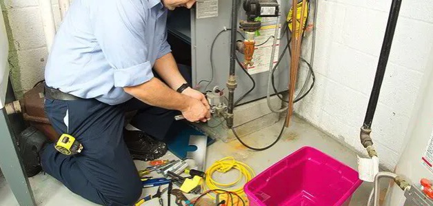Technician kneeling at a furnace making a repair with hand tools