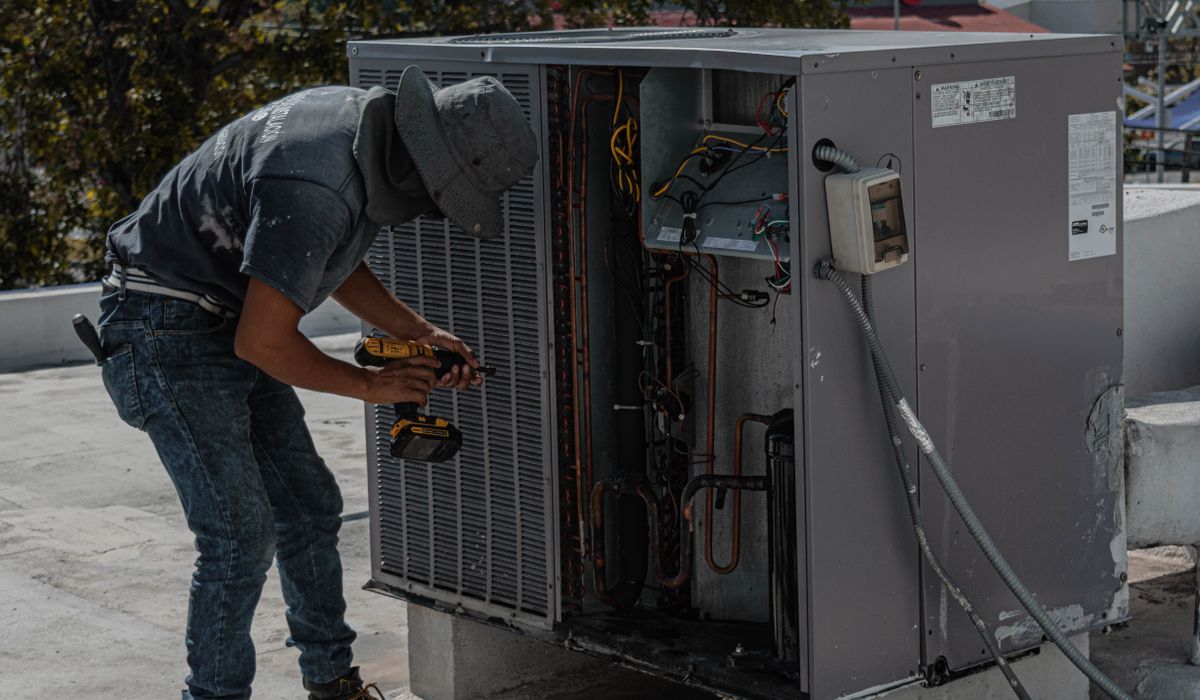 Technician working inside an opened rooftop package unit with a drill